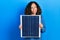 Middle age hispanic woman holding photovoltaic solar panel smiling looking to the side and staring away thinking