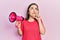 Middle age hispanic woman shouting through megaphone serious face thinking about question with hand on chin, thoughtful about