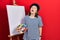 Middle age hispanic woman standing drawing with palette by painter easel stand looking sleepy and tired, exhausted for fatigue and