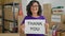 Middle age hispanic woman volunteer smiling confident holding thank you message at charity center