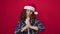 Middle age hispanic woman wearing christmas hat praying and crossing fingers for lucky over isolated red background