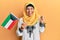 Middle age hispanic woman wearing hijab holding kuwait flag screaming proud, celebrating victory and success very excited with