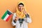 Middle age hispanic woman wearing hijab holding kuwait flag smiling happy and positive, thumb up doing excellent and approval sign