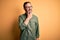 Middle age hoary man wearing casual green shirt and glasses over isolated yellow background with hand on chin thinking about