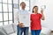 Middle age interracial couple holding recycling bin with plastic bottles at home doing ok sign with fingers, smiling friendly