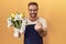 Middle age man with beard florist shop holding flowers beckoning come here gesture with hand inviting welcoming happy and smiling