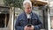 Middle age man with grey hair using smartphone at street