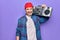 Middle age man wearing cap listening vintage boombox over isolated purple background looking positive and happy standing and