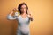 Middle age pregnant woman expecting baby at aged pregnancy holding alarm clock with open hand doing stop sign with serious and