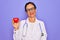 Middle age senior cardiologist doctor woman holding red heart over purple background with a happy face standing and smiling with a