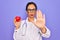 Middle age senior cardiologist doctor woman holding red heart over purple background with open hand doing stop sign with serious