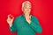 Middle age senior grey-haired man holding romantic red heart object over isolated red background cover mouth with hand shocked