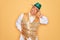 Middle age senior grey-haired man wearing Brazilian carnival custome over yellow background stretching back, tired and relaxed,