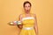 Middle age senior pin up woman wearing 50s style retro dress holding tray with cupcakes scared in shock with a surprise face,