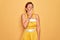 Middle age senior pin up woman wearing 50s style retro dress over yellow background bored yawning tired covering mouth with hand