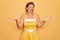 Middle age senior pin up woman wearing 50s style retro dress over yellow background clueless and confused expression with arms and
