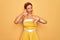 Middle age senior pin up woman wearing 50s style retro dress over yellow background Doing thumbs up and down, disagreement and