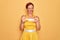 Middle age senior pin up woman wearing 50s style retro dress over yellow background smiling funny doing claw gesture as cat,