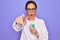 Middle age senior scientist woman wearing laboratory coat holding research test tube pointing with finger to the camera and to