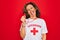 Middle age senior summer lifeguard woman holding whistle over red background sticking tongue out happy with funny expression