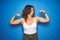 Middle age senior woman with curly hair standing over blue isolated background showing arms muscles smiling proud