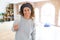 Middle age woman with curly hair smiling cheerful painting new house using paint brush, renovating and decorating the wall