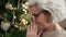 Middle age woman with grey hair sitting by christmas tree praying at home