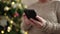 Middle age woman with grey hair using smartphone by christmas tree at home