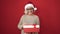 Middle age woman with grey hair wearing christmas hat unpacking gift over isolated red background