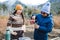 Middle age woman and her young daughter wearing warm clothes, brewing yerba mate at countryside.