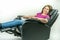 Middle-age woman leaning back in black leather recliner armchair. Checking blood pressure using portable blood pressure machine.