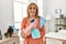 Middle age woman smiling happy holding diffuser and rag standing at home