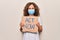Middle age woman wearing coronavirus protection mask holding act now protest cardboard looking positive and happy standing and