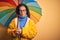 Middle age woman wearing yellow raincoat under colorful umbrella over isolated background with a confident expression on smart