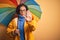 Middle age woman wearing yellow raincoat under colorful umbrella over isolated background with open hand doing stop sign with