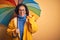 Middle age woman wearing yellow raincoat under colorful umbrella over isolated background surprised with an idea or question