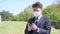 Middle-aged Asian businessman wearing a mask and using a smartphone on the lawn.