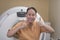 A middle aged asian man brimming with positivity gives two thumbs up, before undergoing a CT scan. At a hospital clinic