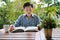 A middle-aged Asian man reading a book resting in the backyard