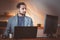 A middle-aged aspiring businessman with a beard works in the evening at home in front of computers