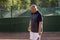 A middle-aged bald man emotionally plays tennis on the court. Loses the opponent. Outdoor.