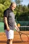 A middle-aged bald man plays tennis on the outdoor court. Sunny day. Vertical