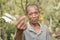 A middle aged and balding rural Filipino man makes a heart finger gesture while outside his home. Declaring his love and approval