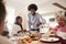 Middle aged black man carving and serving meat at Sunday family dinner with his partner, kids and their grandparents, front view