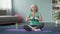 Middle-aged blond female practicing lotus pose at home, doing yoga exercises