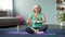 Middle-aged blond female practicing lotus pose at home, doing yoga exercises