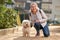 Middle-aged blond woman walking with fluffy white dog in summer city