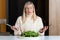 Middle aged blonde woman with dissatisfied facial expression eating salad in the kitchen