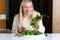 Middle aged blonde woman with dissatisfied facial expression eating salad in the kitchen