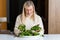 Middle aged blonde woman with dissatisfied facial expression eating salad in the kitchen